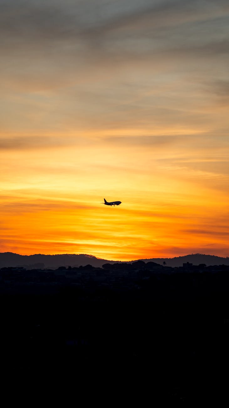 silhouette of a plane flying over sunset sky